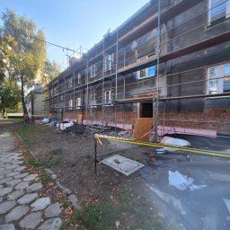 MagBud Rozbiórki,Wyburzenia i Prace ziemne Magdalena Musiał - Budynek w trakcie remontu z rusztowaniami, widoczne ocieplenie, częściowo odsłonięta cegła. Na pierwszym planie gruz i taśma ostrzegawcza.