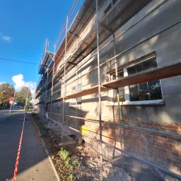 MagBud Rozbiórki,Wyburzenia i Prace ziemne Magdalena Musiał - Budynek w trakcie remontu z rusztowaniem. Częściowo odsłonięta cegła, widoczne okna i niebieskie niebo. Ujęcie z dołu, z perspektywy ulicy.