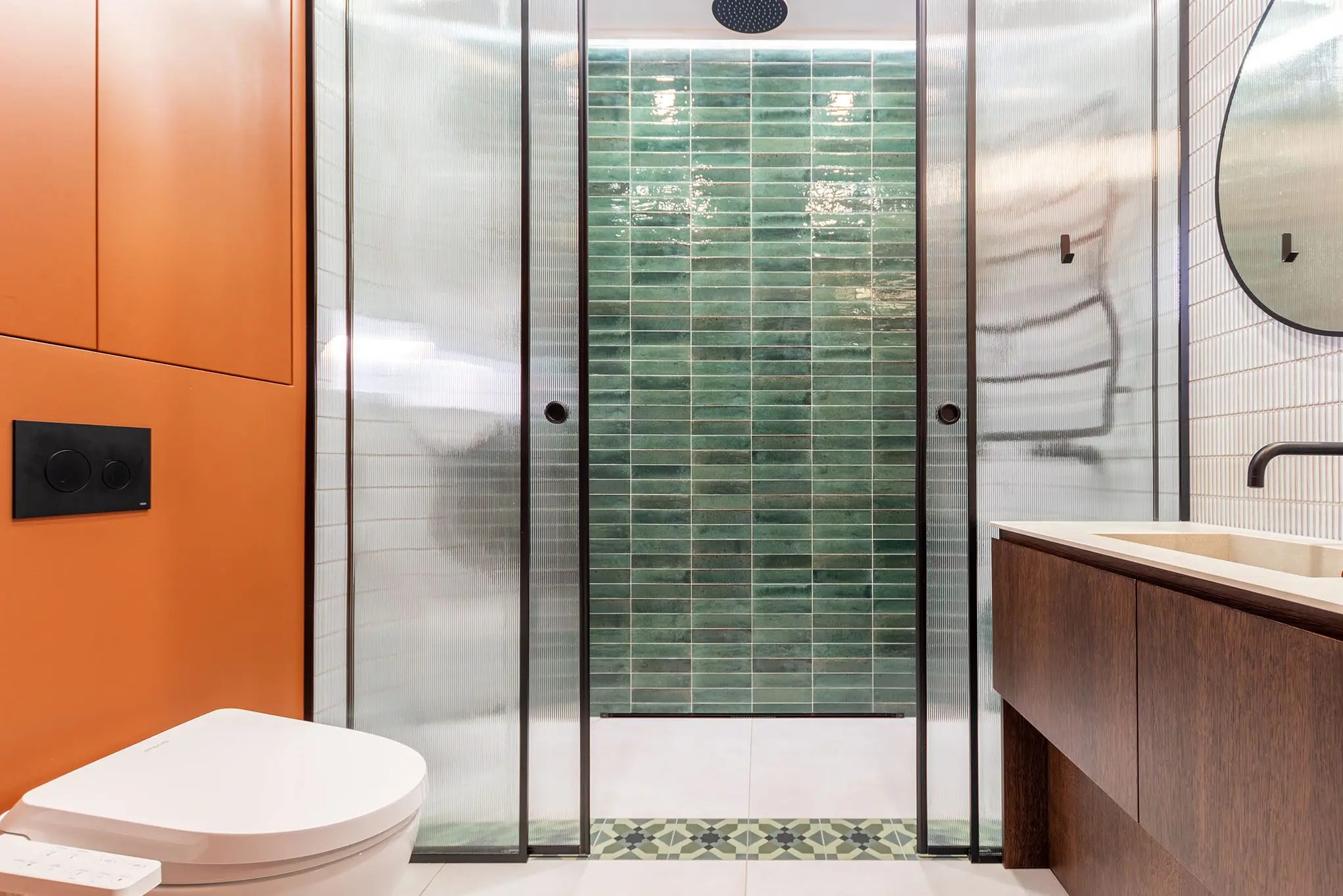 Nowoczesna łazienka z kabiną prysznicową z zielonymi płytkami, umywalką z drewnianą szafką i pomarańczową ścianą z toaletą. Wnętrze po remoncie.