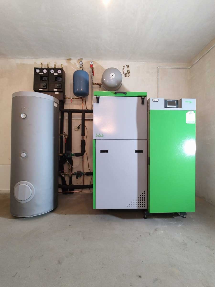 Nowoczesny piec na paliwo stałe SAS w kotłowni w Kielcach. Szary zbiornik buforowy i zielony korpus pieca. Instalacja CO z rur miedzianych i czarnych.