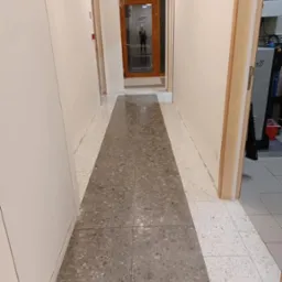 Wypolerowana, szara posadzka w korytarzu biurowym w Toruniu. Widok na czyste, błyszczące płytki i drzwi w tle. Dbałość o detale i wysoki standard.