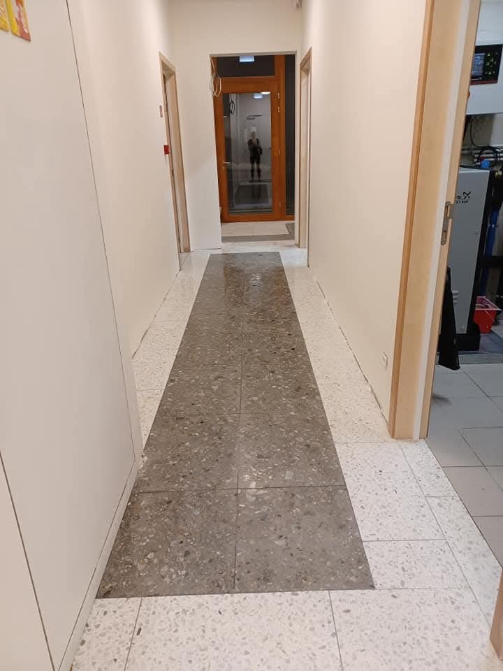 Wypolerowana, szara posadzka w korytarzu biurowym w Toruniu. Widok na czyste, błyszczące płytki i drzwi w tle. Dbałość o detale i wysoki standard.