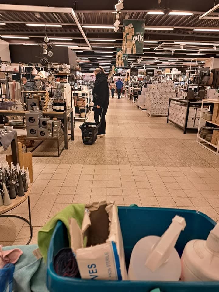 Wózek z detergentami na tle wnętrza sklepu. Widoczny fragment podłogi po umyciu. Perspektywa z dołu, sugerująca pracę w trakcie wykonywania.