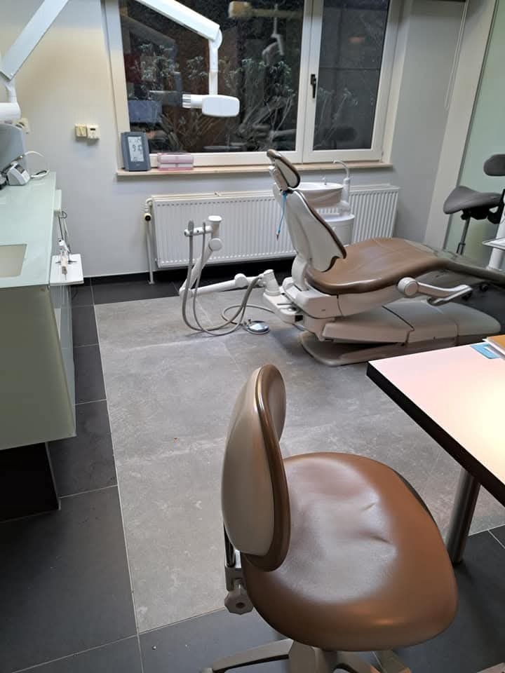 Wnętrze gabinetu stomatologicznego: fotel dentystyczny z brązowym siedziskiem, białe meble i okno z widokiem na zieleń. Nowoczesne, minimalistyczne wykończenie.