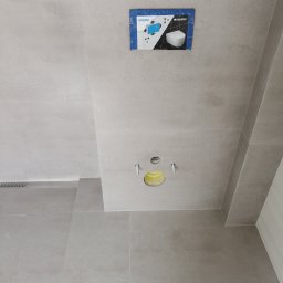 House-Serwis Ireneusz Korzeniewski - Szara łazienka w trakcie montażu podtynkowego stelaża WC Geberit Sigma, widoczne płytki, otwory na przyłącza i instrukcja montażu na ścianie.