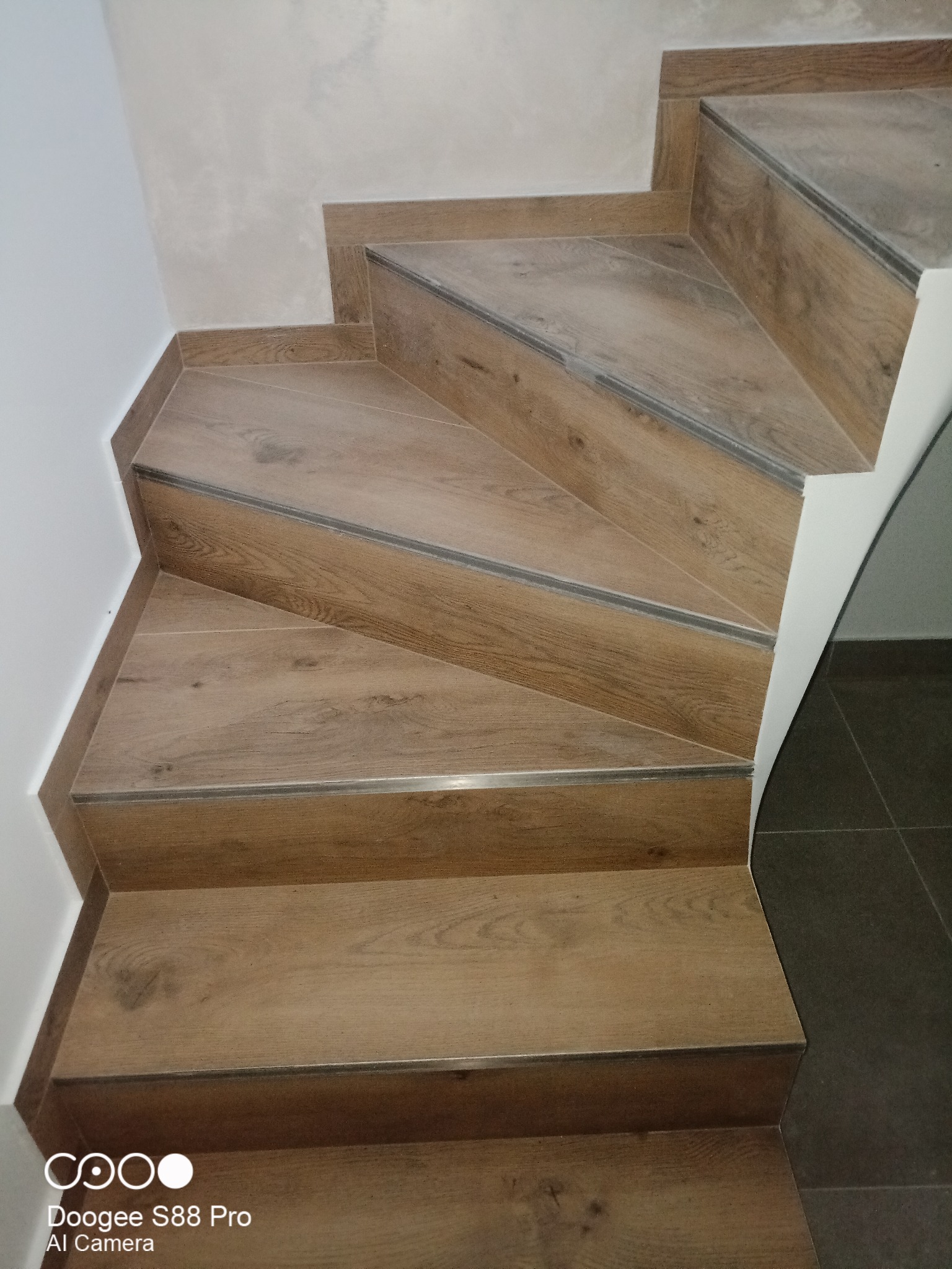 Wykończone schody z okładziną imitującą drewno, z metalowymi listwami na krawędziach stopni, widok z góry na fragment klatki schodowej.