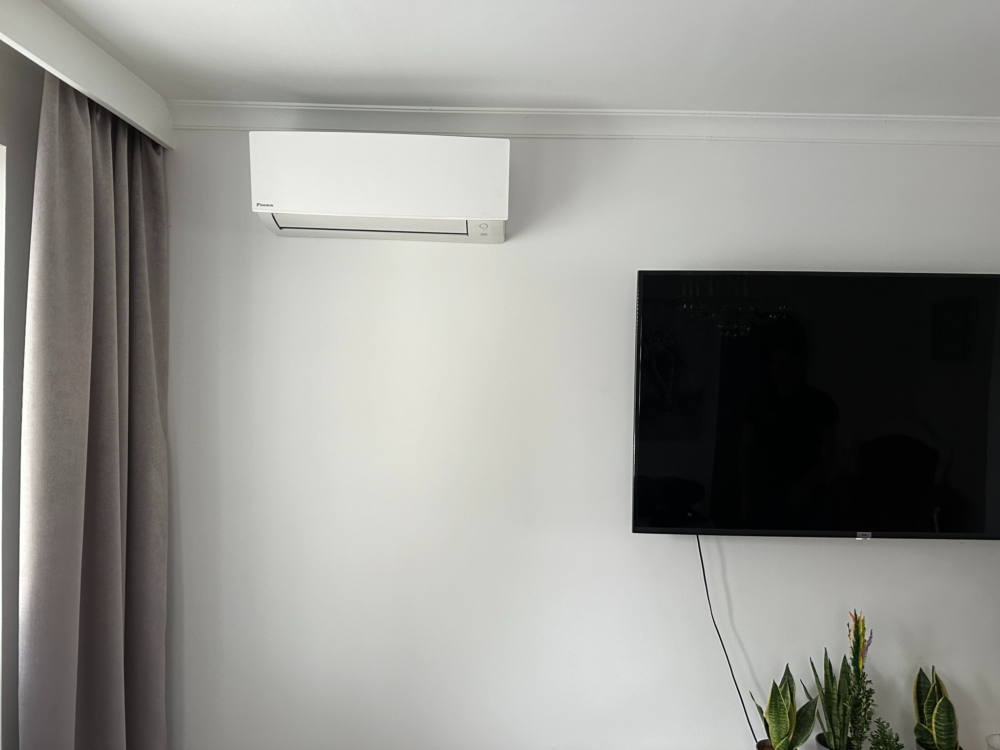 Biała klimatyzacja Daikin zamontowana na ścianie w salonie w Makowie Mazowieckim. Obok telewizor i zasłony. Nowoczesny design, czyste linie.