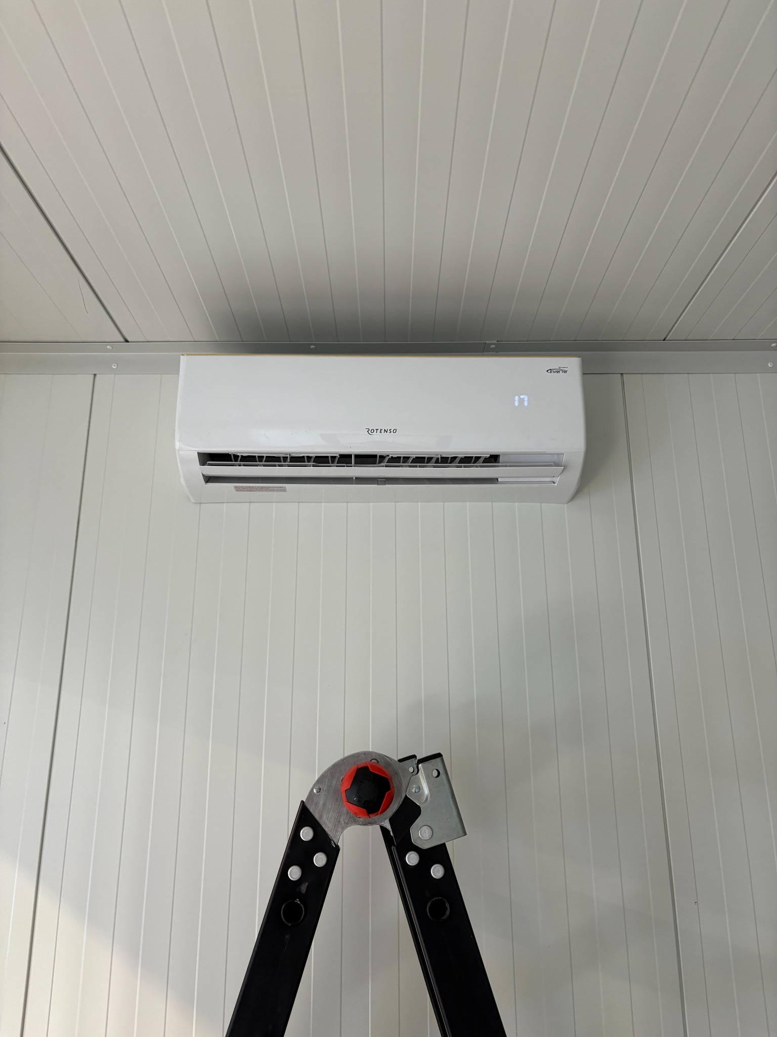 Biały klimatyzator ROTENSO zamontowany na ścianie z paneli, widoczny fragment drabiny, wskazujący na niedawny montaż lub serwis.