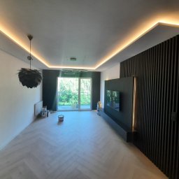 BestRefit - Stylowe wykończenie wnętrza w Częstochowie: parkiet w jodełkę, czarna ściana z lamelami i podświetlany sufit. Widoczne puszki po farbie.