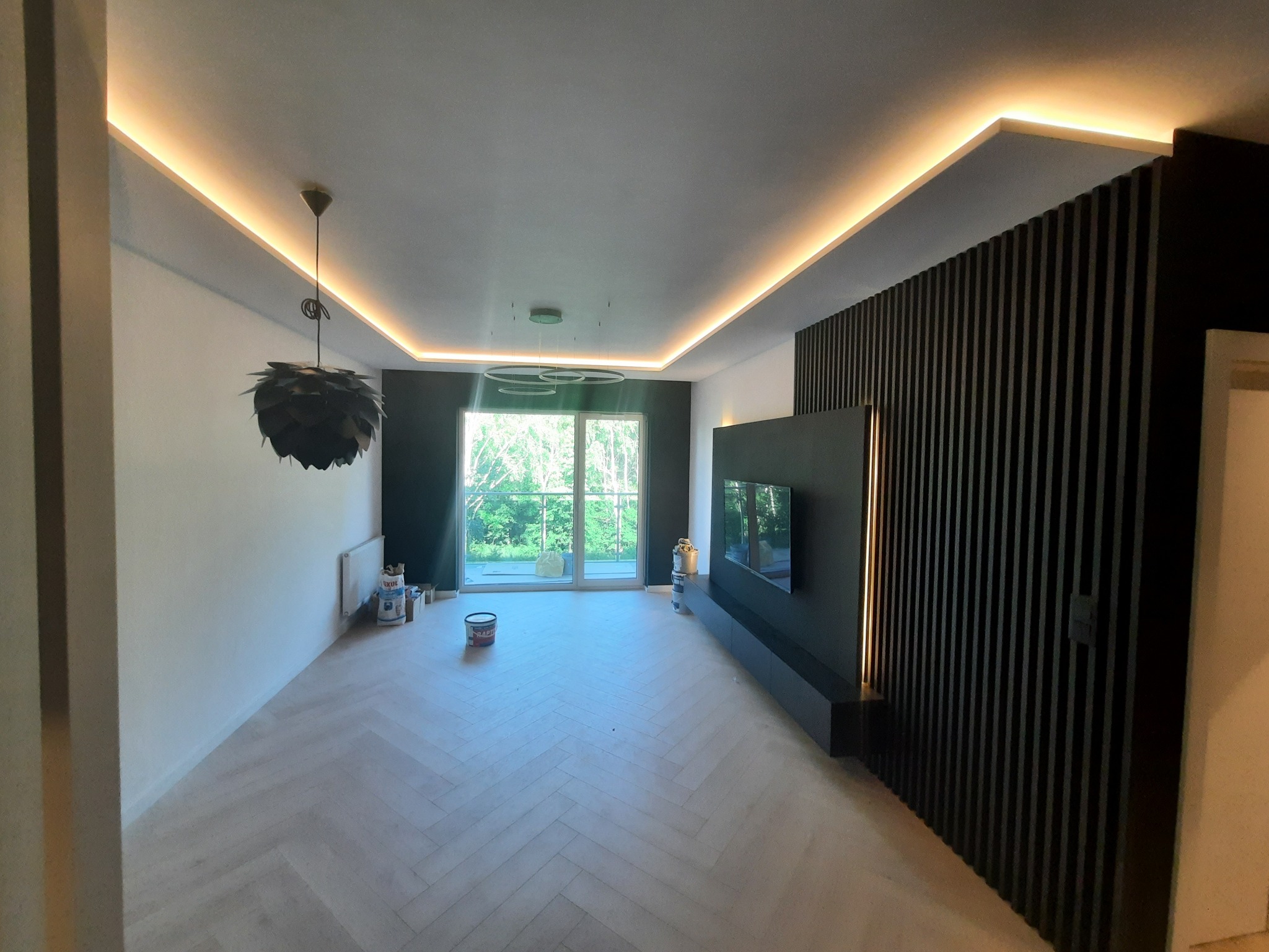 Stylowe wykończenie wnętrza w Częstochowie: parkiet w jodełkę, czarna ściana z lamelami i podświetlany sufit. Widoczne puszki po farbie.