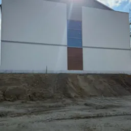 Nowoczesny dom z białą elewacją, drewnianym akcentem i trzema oknami. Słońce w kadrze. Widoczne rusztowanie. Teren wokół domu w stanie surowym.