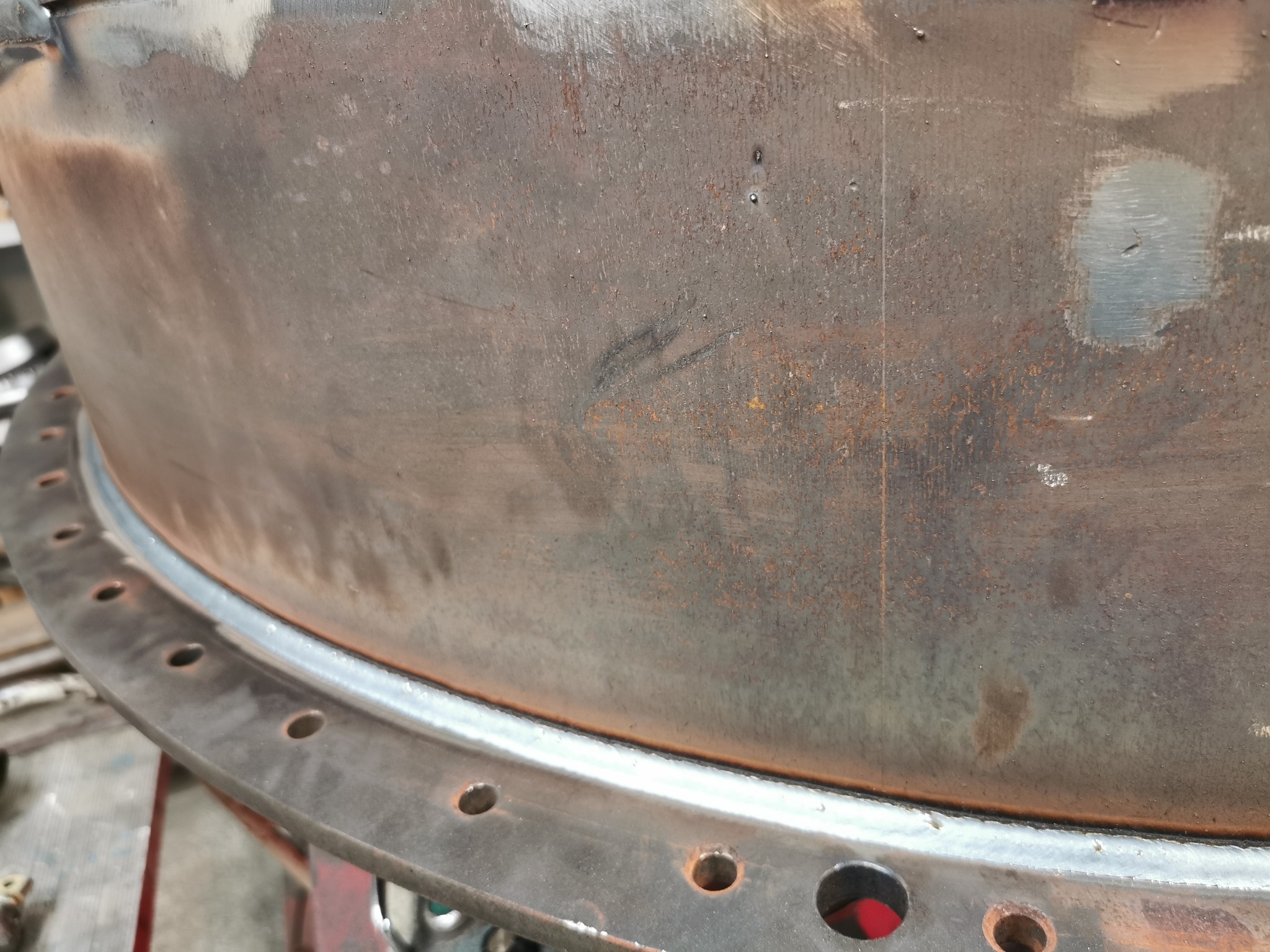 Spoina obwodowa na elemencie konstrukcji stalowej z otworami, wykonana w Bolesławcu. Widoczne ślady obróbki i patyna na powierzchni metalu.