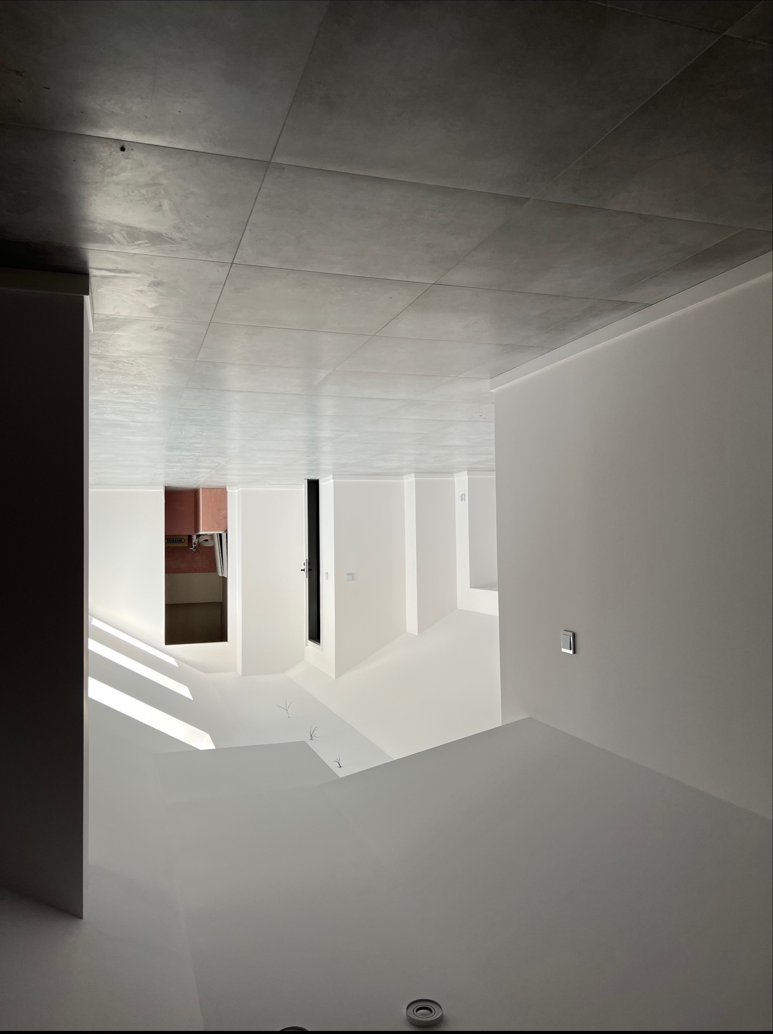Nowoczesne wykończenie wnętrza z szarymi płytkami na suficie i białymi ścianami. Widoczne wnęki i minimalistyczne oświetlenie.