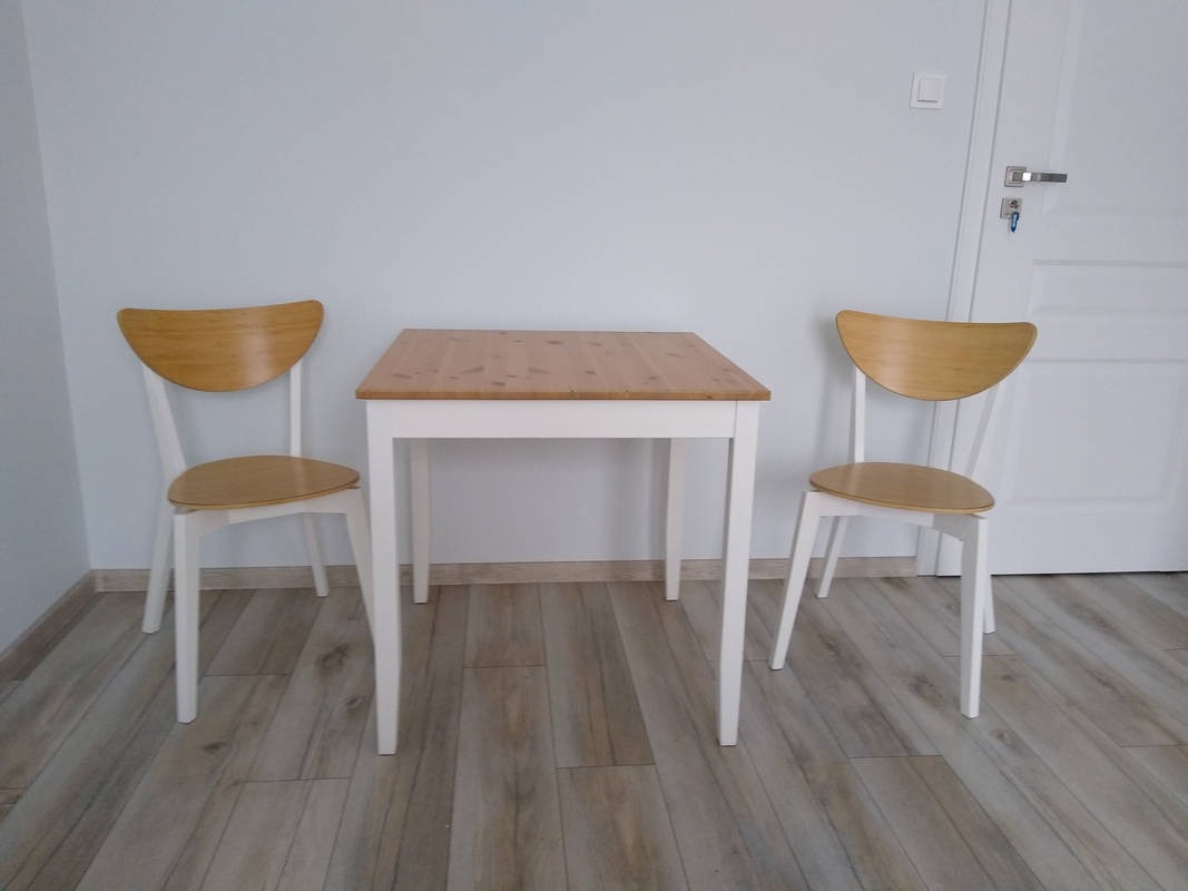 Komplet: drewniany stół z blatem w naturalnym odcieniu i dwa krzesła z jasnego drewna, ustawione na panelach podłogowych w minimalistycznym wnętrzu.