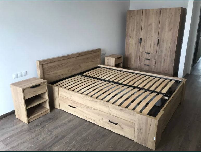 Komplet mebli do sypialni: łóżko z szufladami, szafki nocne i duża szafa z frontami w kolorze drewna, ustawione w jasnym pokoju na drewnianej podłodze.