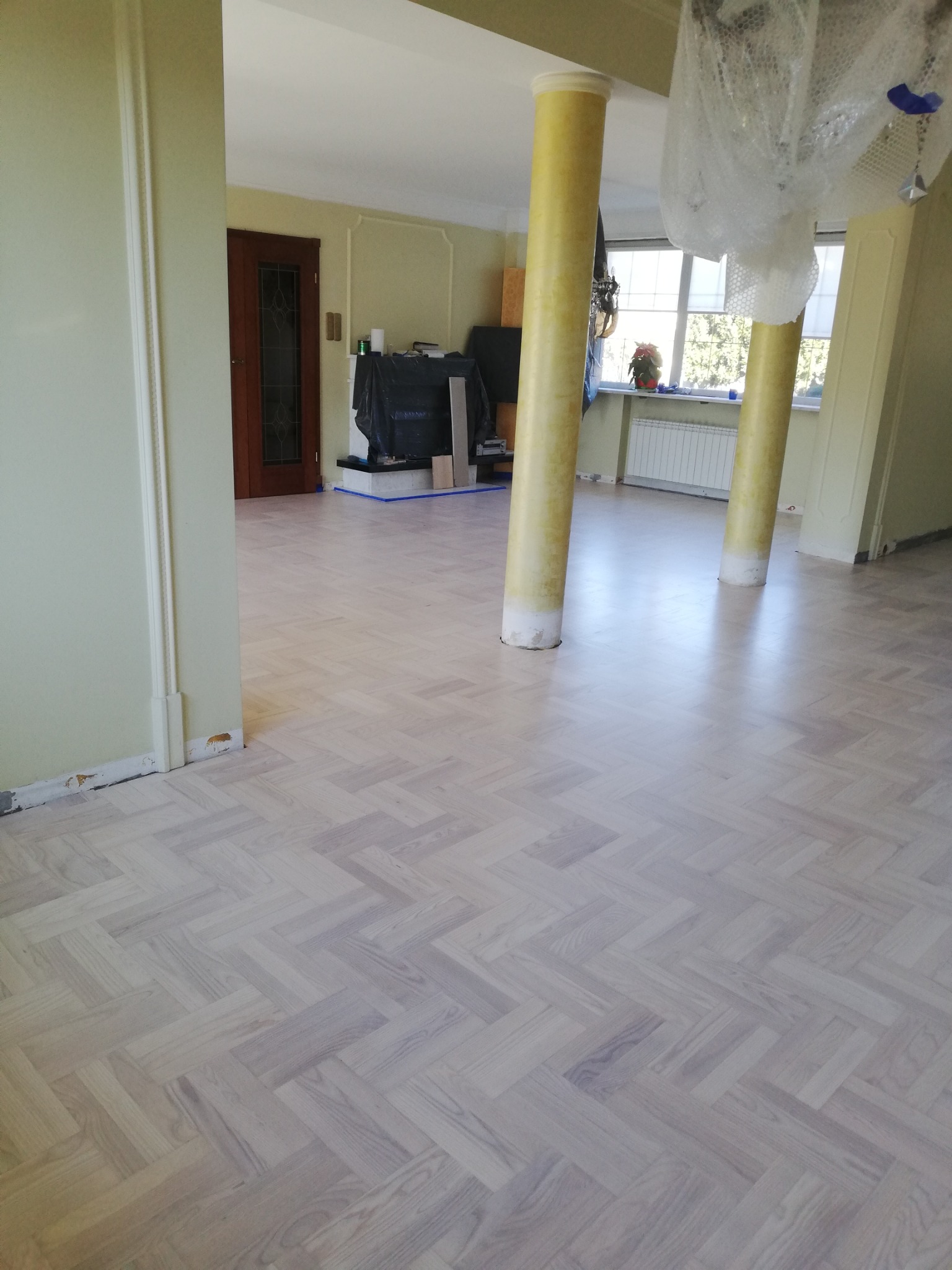 Jasna podłoga parkietowa ułożona w jodełkę w przestronnym wnętrzu z kolumnami. Widoczne przygotowania do dalszych prac wykończeniowych.
