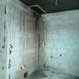 Bartosz Pękala usługi Elektryczne. Usługi Ogrodnicze - Wnętrze w surowym stanie z widoczną, rozprowadzoną instalacją elektryczną w białych rurkach, prowadzoną po ścianach z betonu komórkowego i suficie.