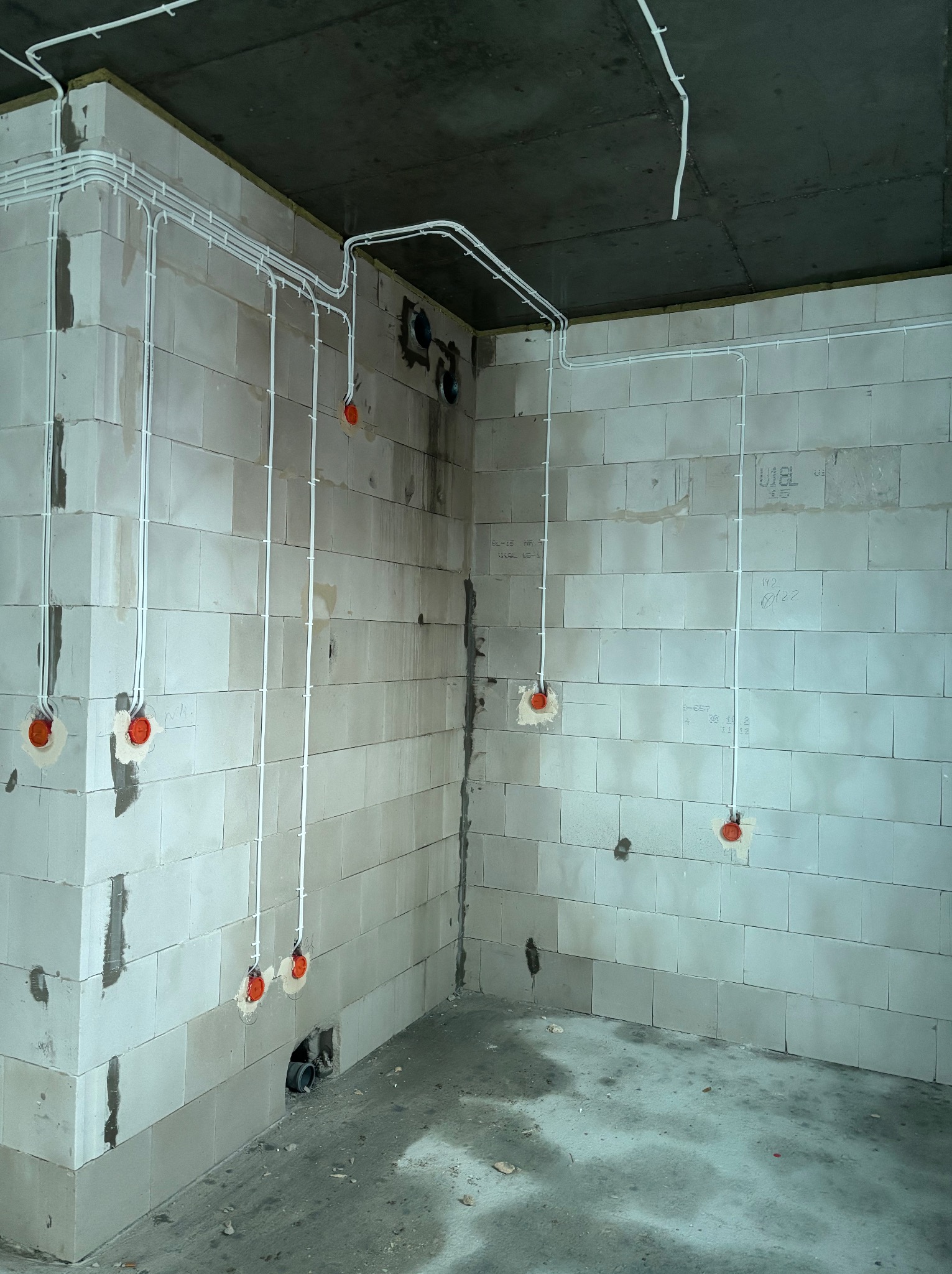 Wnętrze w surowym stanie z widoczną, rozprowadzoną instalacją elektryczną w białych rurkach, prowadzoną po ścianach z betonu komórkowego i suficie.