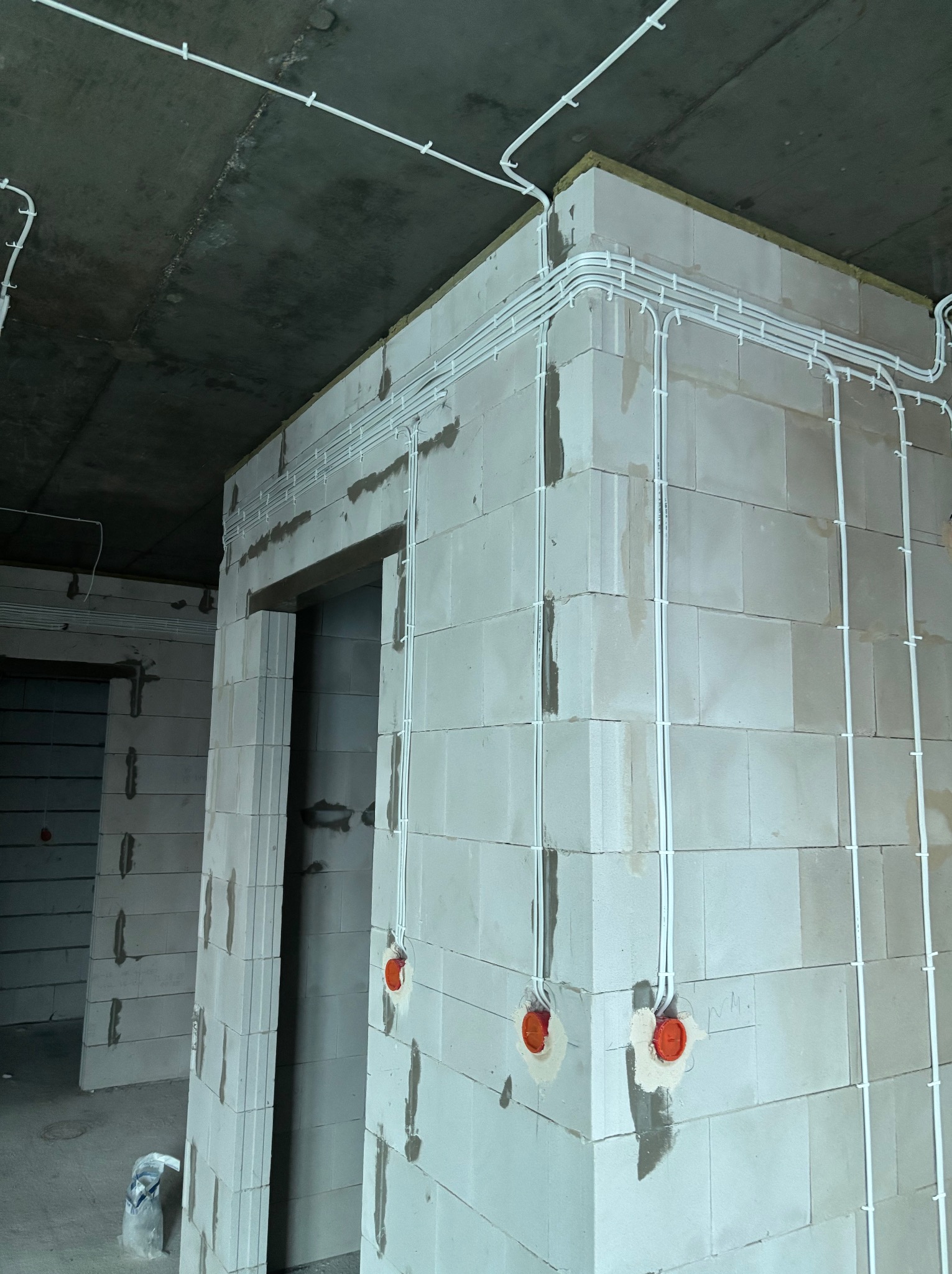 Białe kable elektryczne prowadzone po ścianach z betonu komórkowego, widoczne puszki instalacyjne. Surowy stan wykończenia wnętrza.