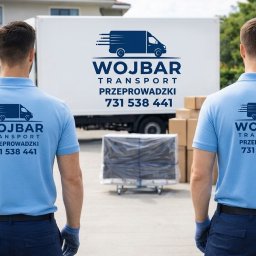 Martin Waliczek - Dwóch pracowników firmy przeprowadzkowej w niebieskich koszulkach z logo na tle samochodu dostawczego i kartonów. Widok z tyłu, skupienie na logo firmy.