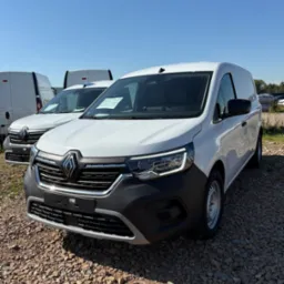 Nowy, biały Renault Kangoo Van z salonu w Krakowie, zaparkowany na żwirowym placu. Widoczne inne busy w tle i błękitne niebo.