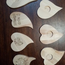 TRANSI P.U.H. - Drewniane serca z wygrawerowanymi napisami 'Miłego dnia', 'Love You' i logo, niektóre z otworem, na ciemnym, drewnianym tle. Rękodzieło.