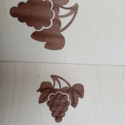 TRANSI P.U.H. - Drewniana płyta z wygrawerowanymi wzorami winogron i napisem 'APATSAGI A.D. 996'. Jasne tło, brązowe motywy. Precyzyjne wykonanie, widoczne detale.