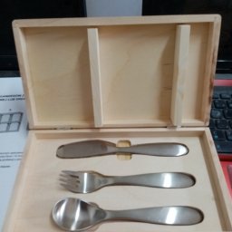 TRANSI P.U.H. - Drewniane pudełko z wyprofilowanym wnętrzem na sztućce: nóż, widelec i łyżka. Precyzyjna obróbka CNC drewna. Światło odbija się od metalowych sztućców.