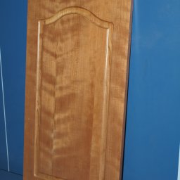 TRANSI P.U.H. - Lakierowany, drewniany front meblowy z ozdobnym frezem, oparty o niebieską ścianę. Widoczna struktura drewna i detale wykończenia.