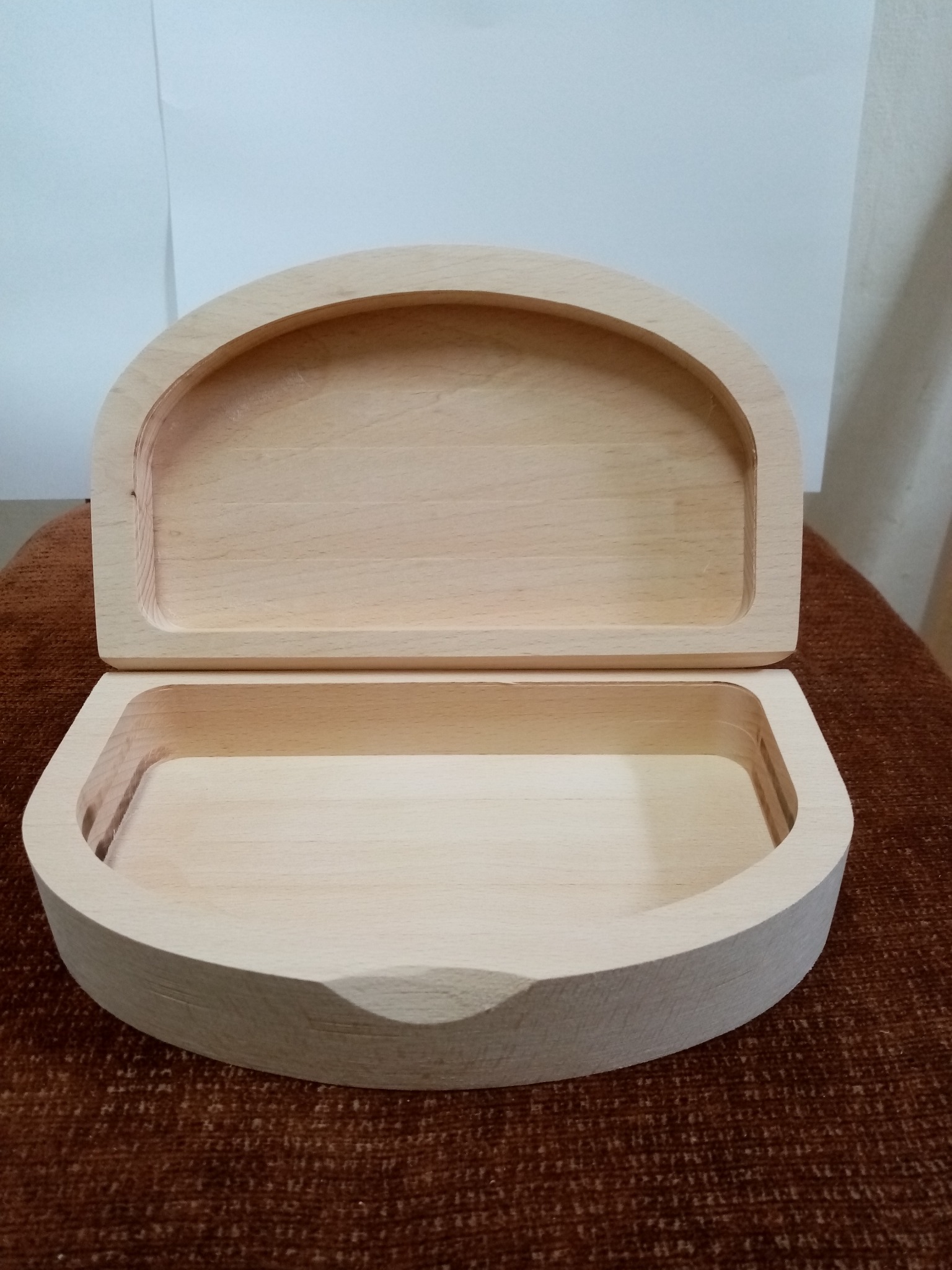 Otwarta, surowa, drewniana szkatułka z zaokrąglonym wiekiem i dnem, ukazująca naturalny rysunek drewna na brązowym tle. Widoczny wewnętrzny kształt.