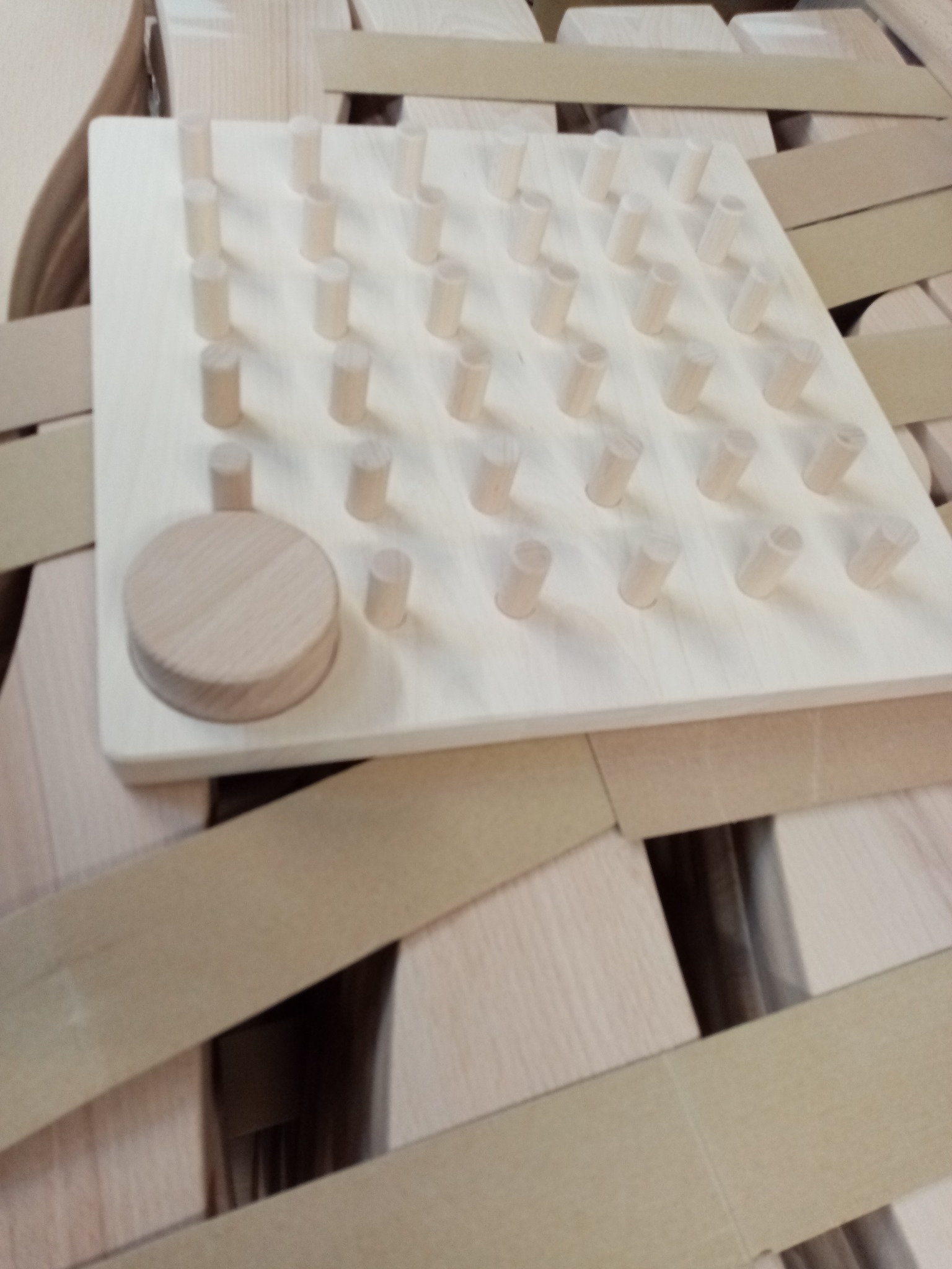 Drewniana płyta z rzędami kołków i okrągłym elementem, całość w jasnych odcieniach drewna, ułożona na konstrukcji z drewnianych listew.