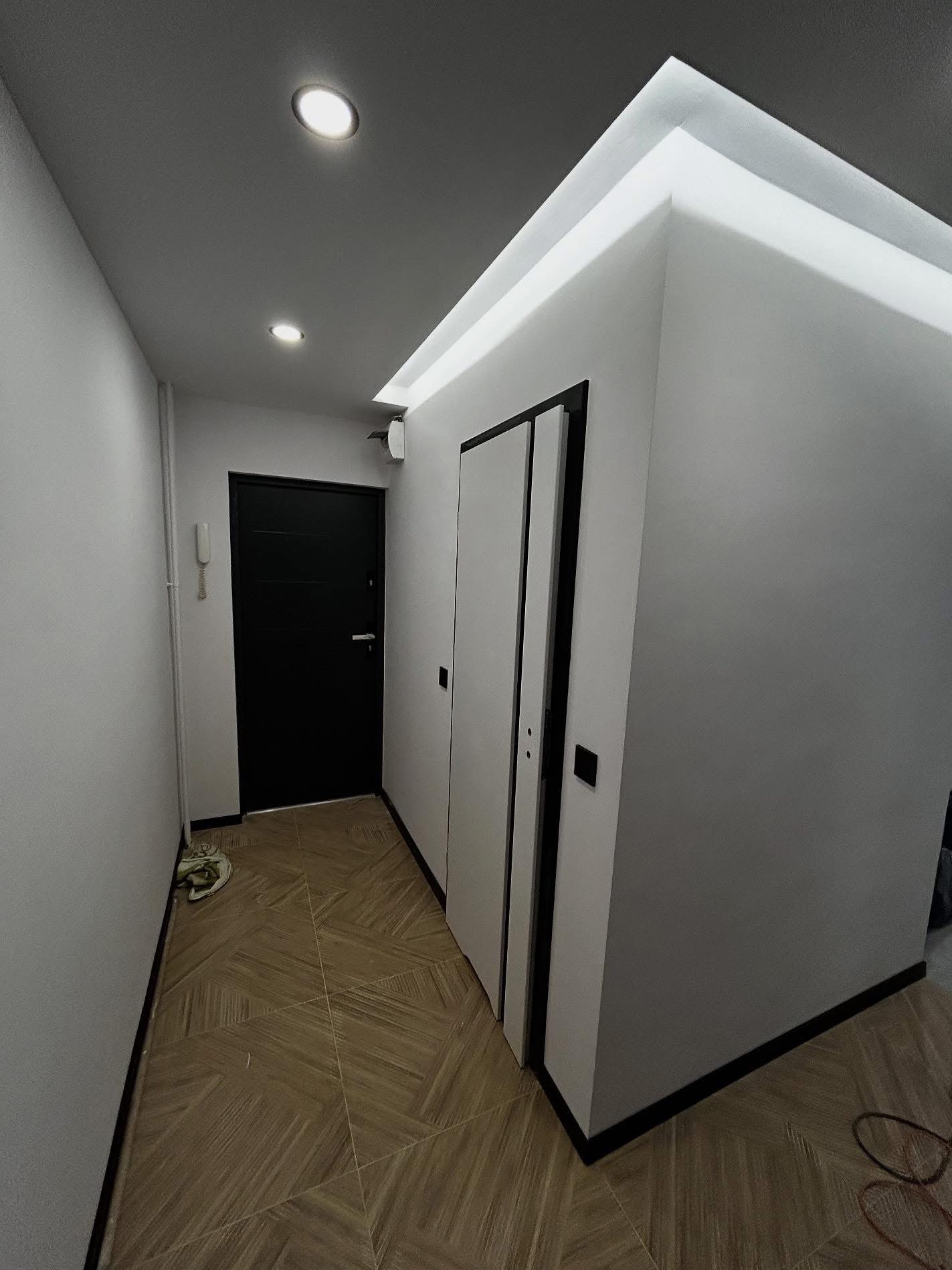 Nowoczesny korytarz z drewnopodobną podłogą, czarnymi drzwiami i białymi ścianami z oświetleniem LED. Minimalistyczny design, widok z dołu.