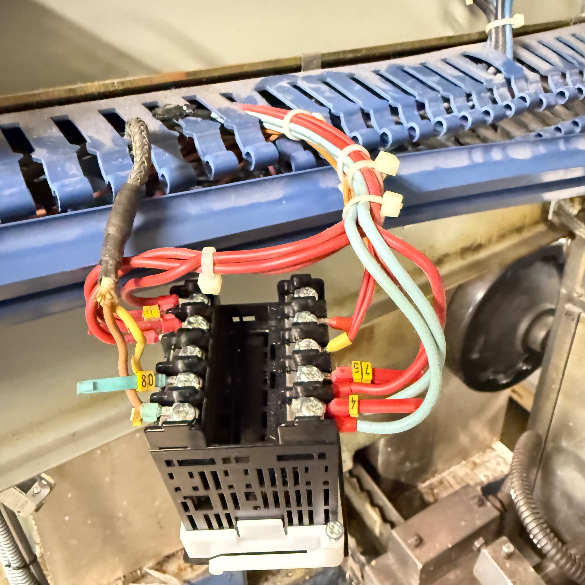 Czarny przekaźnik z kolorowymi kablami oznaczonymi numerami, umieszczony w przemysłowej szafie sterowniczej, z widocznymi elementami instalacji elektrycznej.