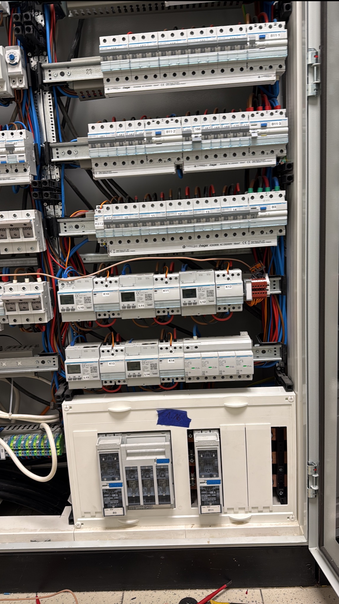 Rozdzielnica elektryczna z licznymi bezpiecznikami i przewodami, widok z bliska, ukazujący skomplikowaną instalację wewnątrz szafy sterowniczej.