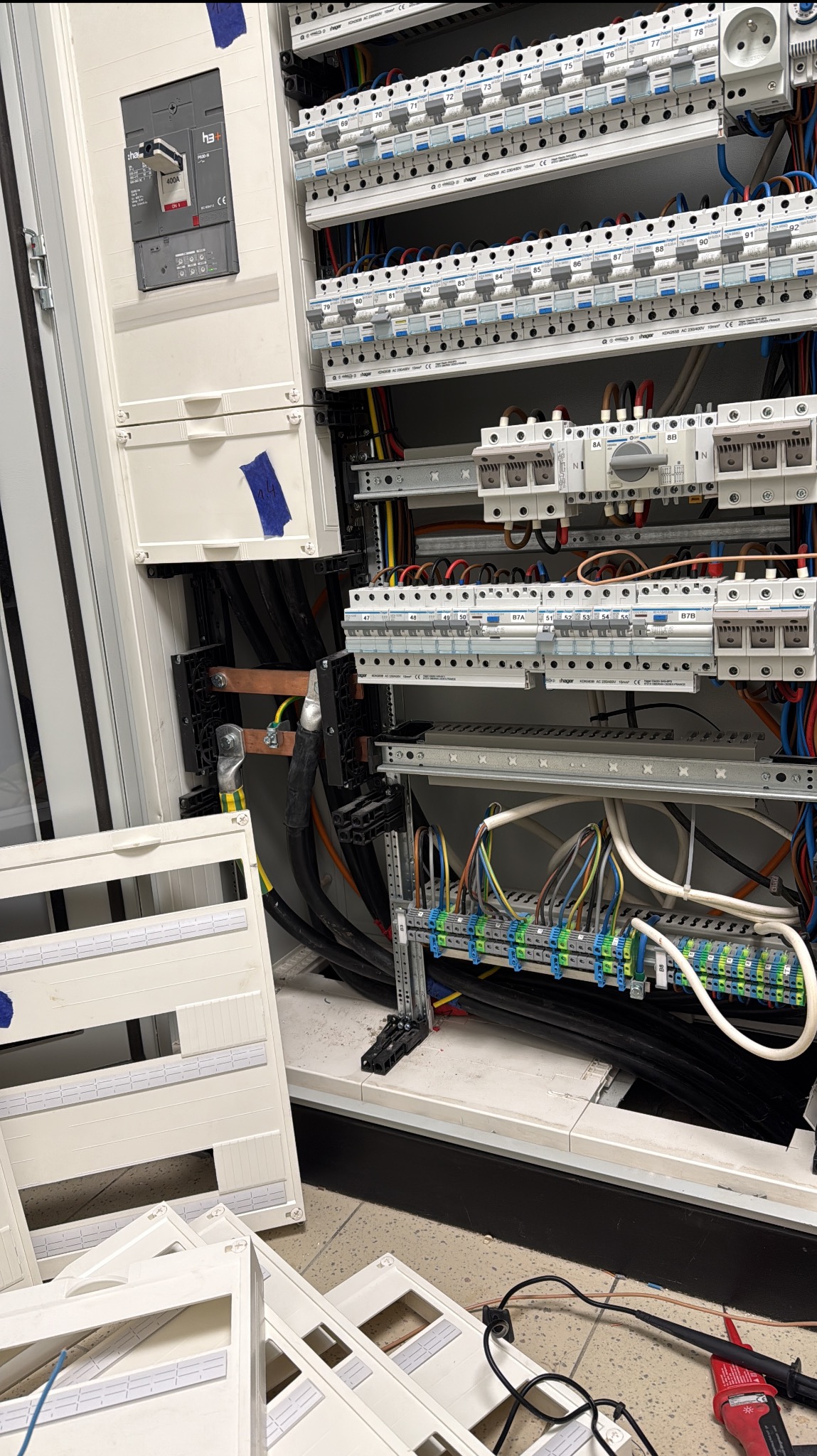 Rozdzielnica elektryczna w trakcie montażu, widoczne kable, bezpieczniki i listwy zaciskowe. Częściowo zamontowane panele obudowy leżą na podłodze.