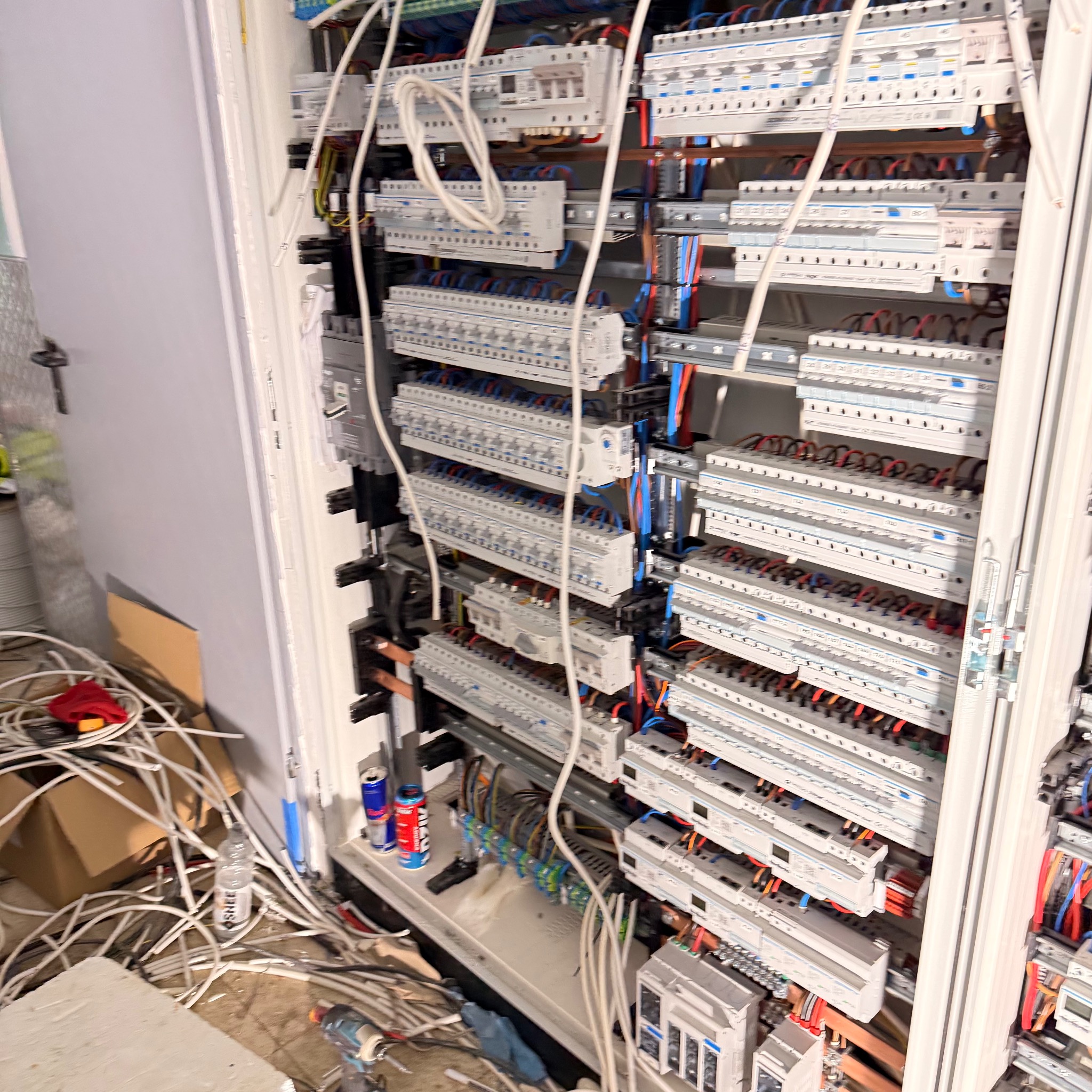 Rozdzielnica elektryczna z licznymi zabezpieczeniami i przewodami. Widoczne kable, puszki i narzędzia. Instalacja w trakcie montażu, wnętrze szafy rozdzielczej.