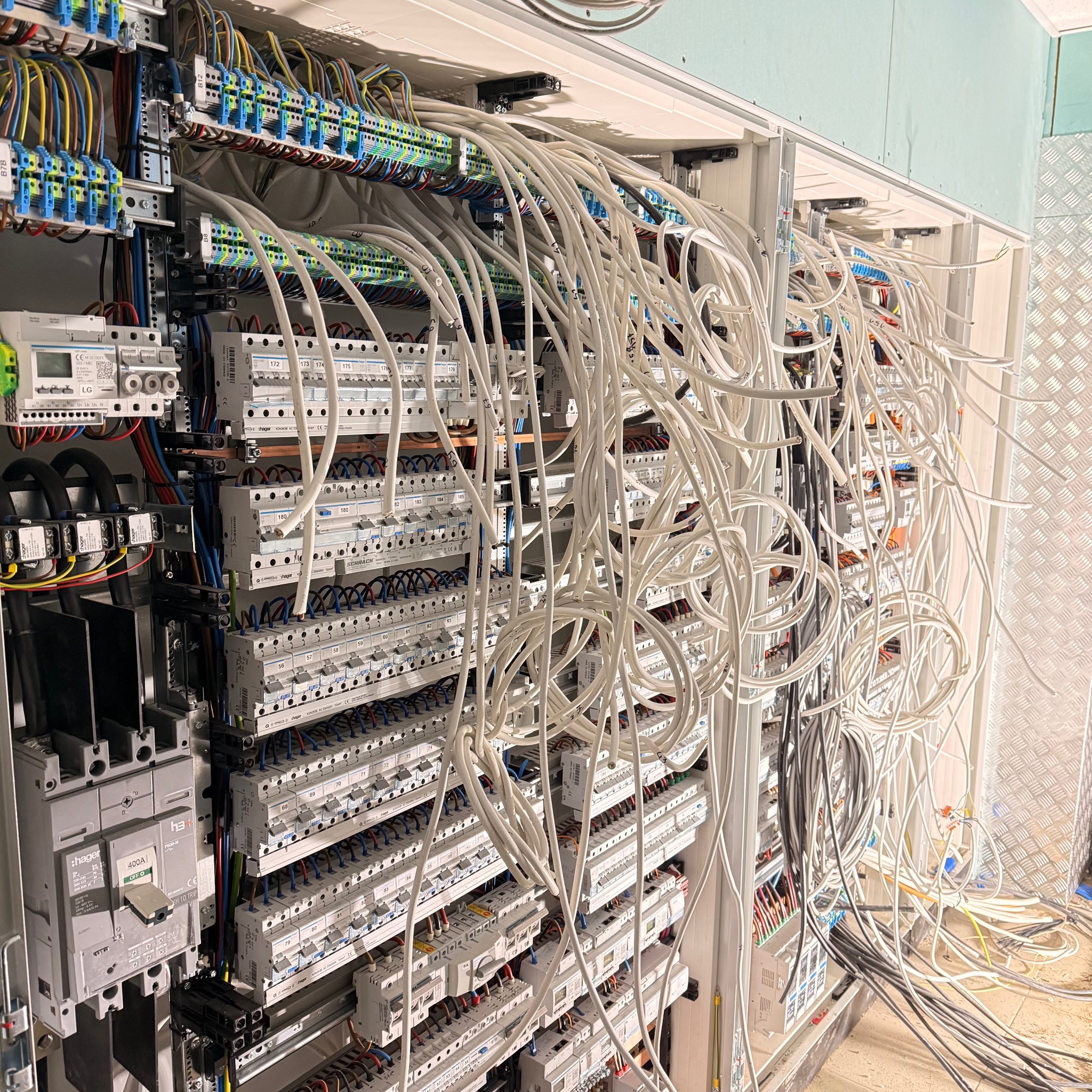 Rozdzielnica elektryczna w trakcie montażu: liczne przewody, bezpieczniki i aparatura modułowa. Widoczne elementy instalacji w surowym stanie.