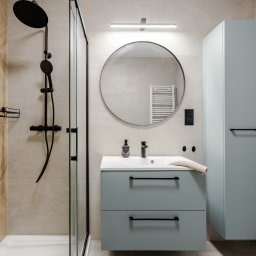 CELMAR Maciej Manelski - Nowoczesna łazienka z kabiną prysznicową typu walk-in, okrągłym lustrem z podświetleniem i szafką umywalkową w odcieniach błękitu z czarnymi akcentami.