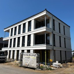 Mykhailo Marusiak - Nowoczesny, trzypiętrowy budynek z białymi elewacjami i czarnymi oknami, w trakcie wykończenia. Widoczny baner firmy 'Thomas Berghoff Elektrotechnik'.