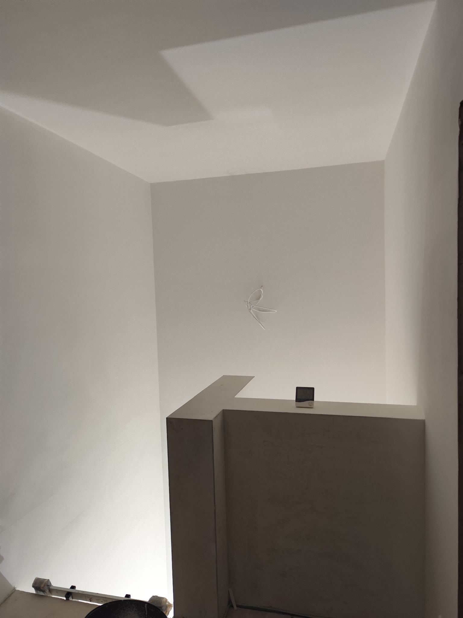 Wnętrze po szpachlowaniu: gładkie, białe ściany i sufit, widoczne przewody elektryczne, czujnik na półce. Minimalistyczny, surowy wygląd.