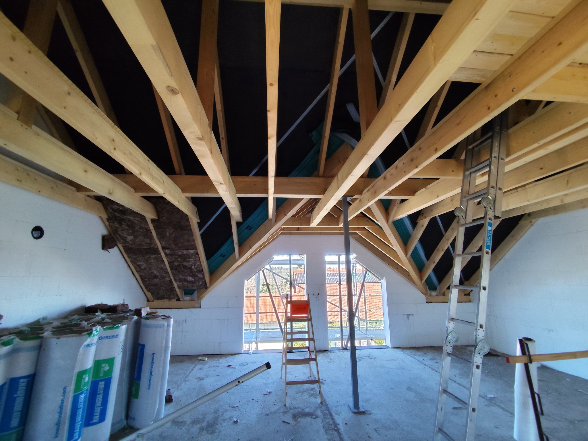 Poddasze w trakcie adaptacji: widoczne drewniane krokwie, izolacja, okna dachowe i drabiny. Przygotowanie do wykończenia wnętrza.