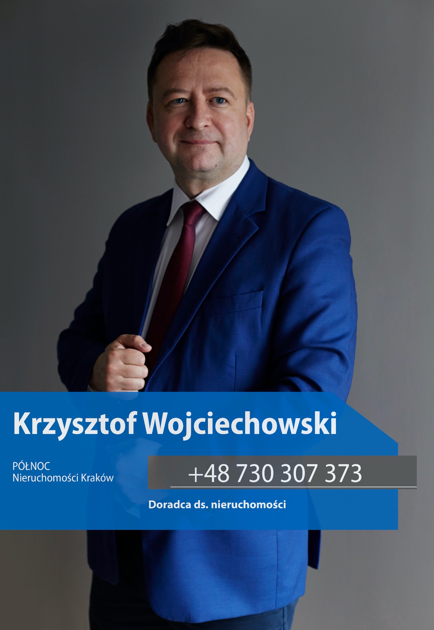 Portret Krzysztofa Wojciechowskiego, doradcy ds. nieruchomości z Krakowa, w niebieskim garniturze i czerwonym krawacie, na szarym tle. Widoczny numer telefonu.