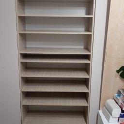 PPHU FARAM - Jasna, drewniana szafa wnękowa z półkami, wbudowana w ścianę. Widoczne panele podłogowe i fragment białej komody z boku. Prosta, minimalistyczna forma.