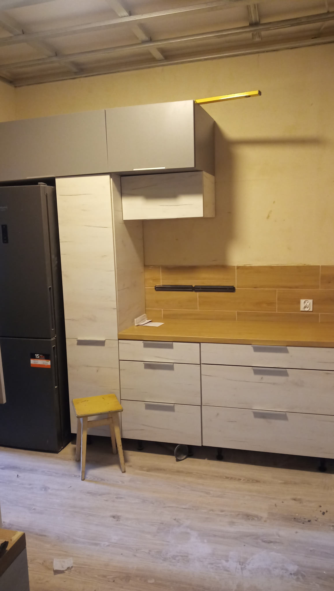 Częściowo zamontowana kuchnia na wymiar z szarymi i drewnopodobnymi frontami, widoczny fragment sufitu podwieszanego i poziomica na górnej szafce.