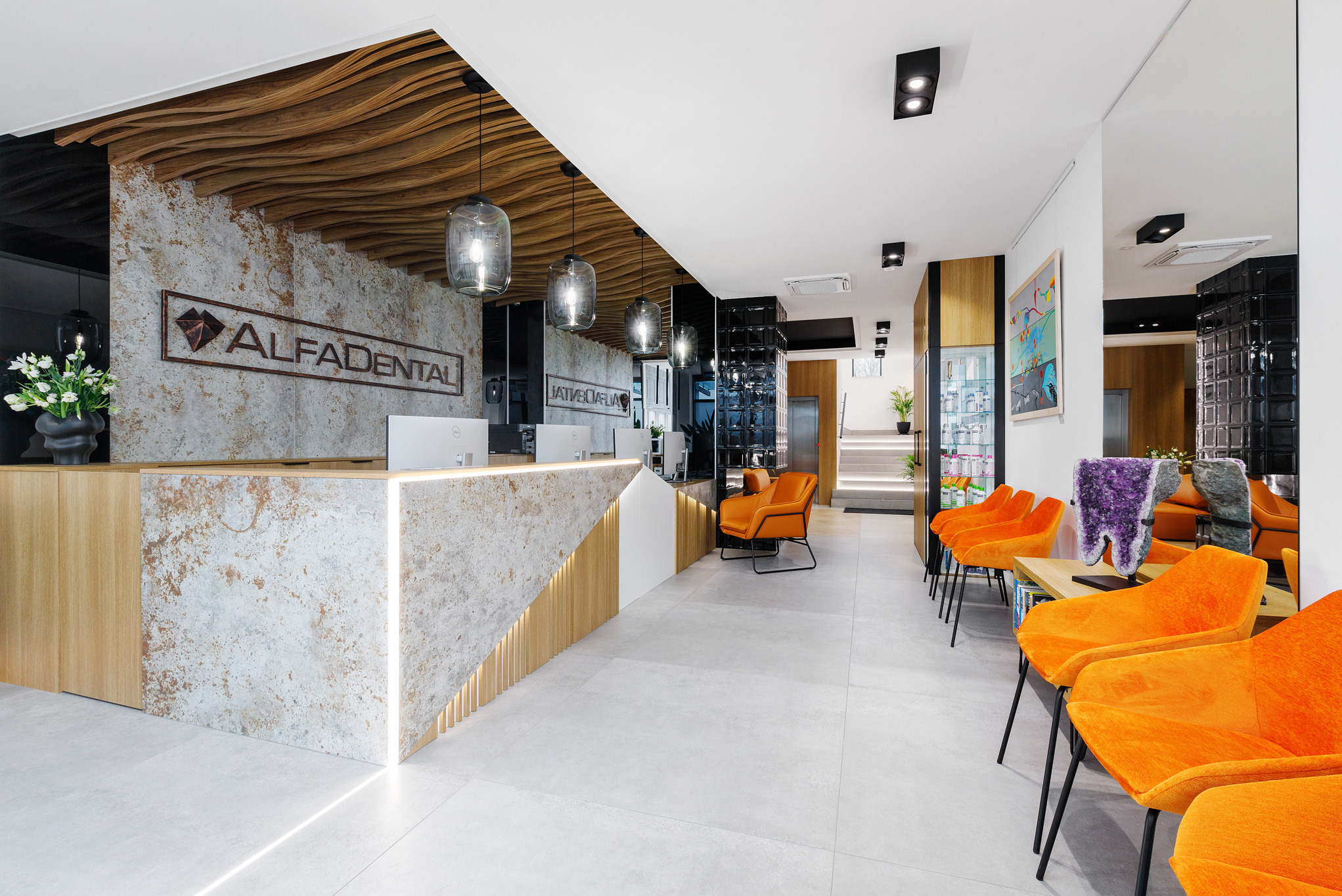 Nowoczesna recepcja Alfa Dental z kamiennym blatem, drewnianym sufitem i pomarańczowymi krzesłami. Widok na jasne wnętrze z roślinami i schodami.