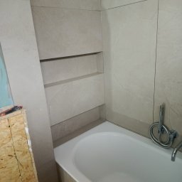 PPK PERFEKT 22 - Wykończona łazienka z wanną i wnęką w beżowych płytkach. Widoczny fragment obudowy w trakcie prac. Bateria wannowa chromowana.