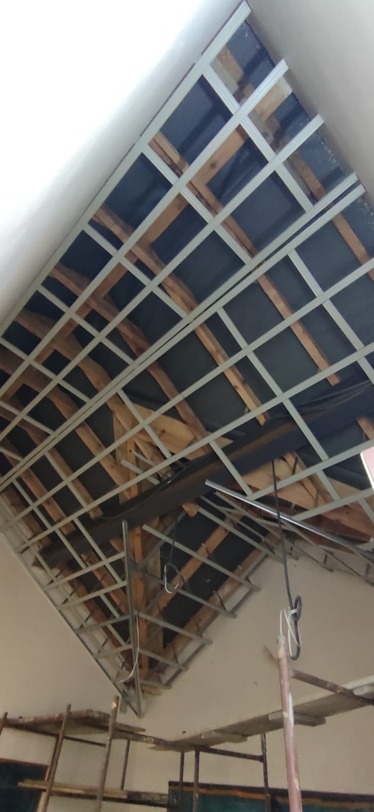 Szkielet sufitu podwieszanego z metalowych profili i drewnianych elementów, widok z dołu, częściowo widoczne rusztowania.