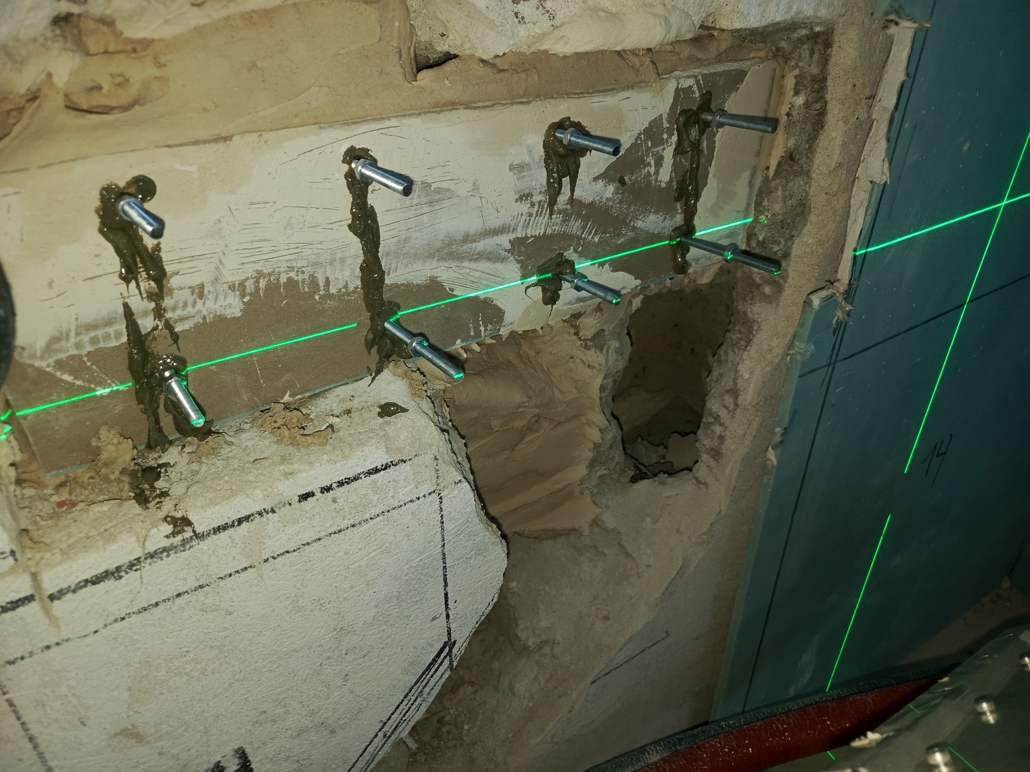Mocowanie płyty karton-gips do ściany z użyciem kotew i lasera krzyżowego, ukazujące precyzję montażu i przygotowanie do dalszych prac wykończeniowych.