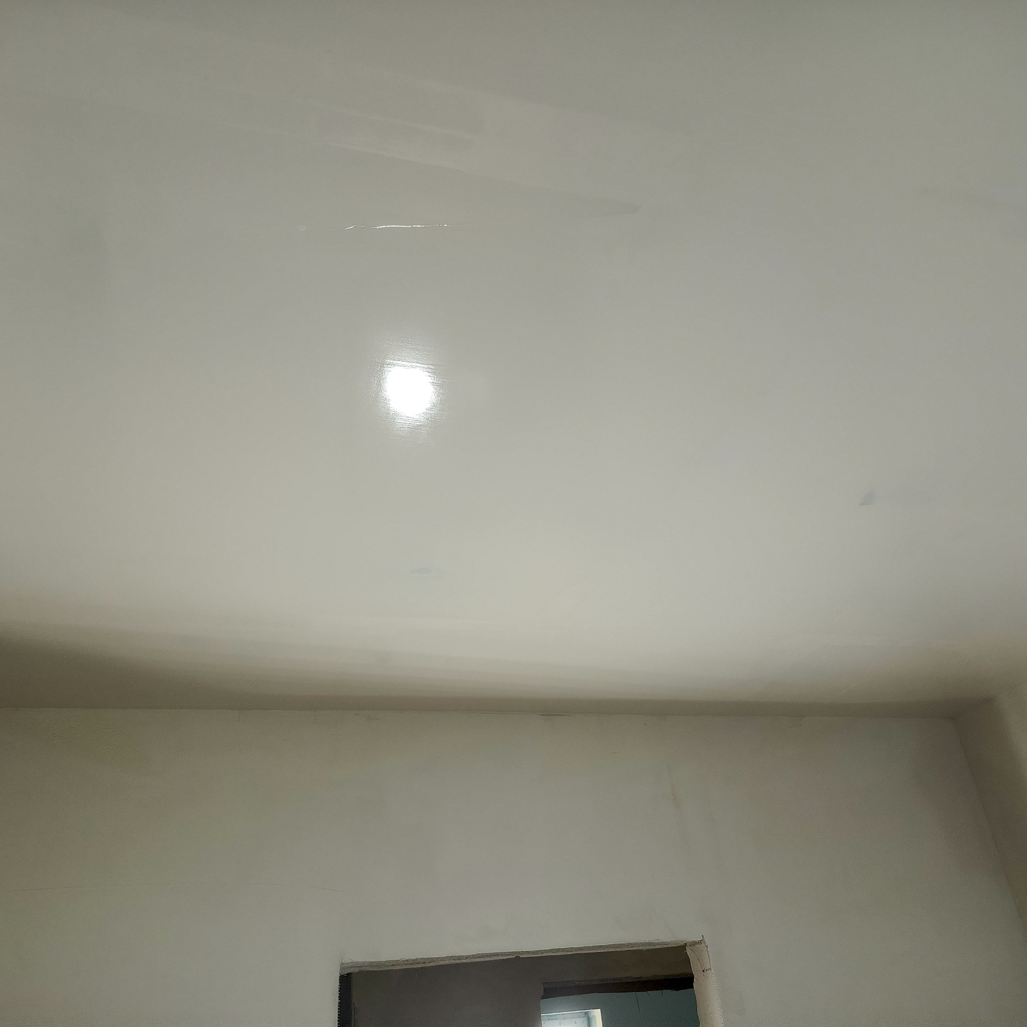 Świeżo pomalowany, biały sufit z widocznym odbiciem światła, fragment ściany i otwór drzwiowy w trakcie wykańczania. Minimalistyczne ujęcie wnętrza po malowaniu.