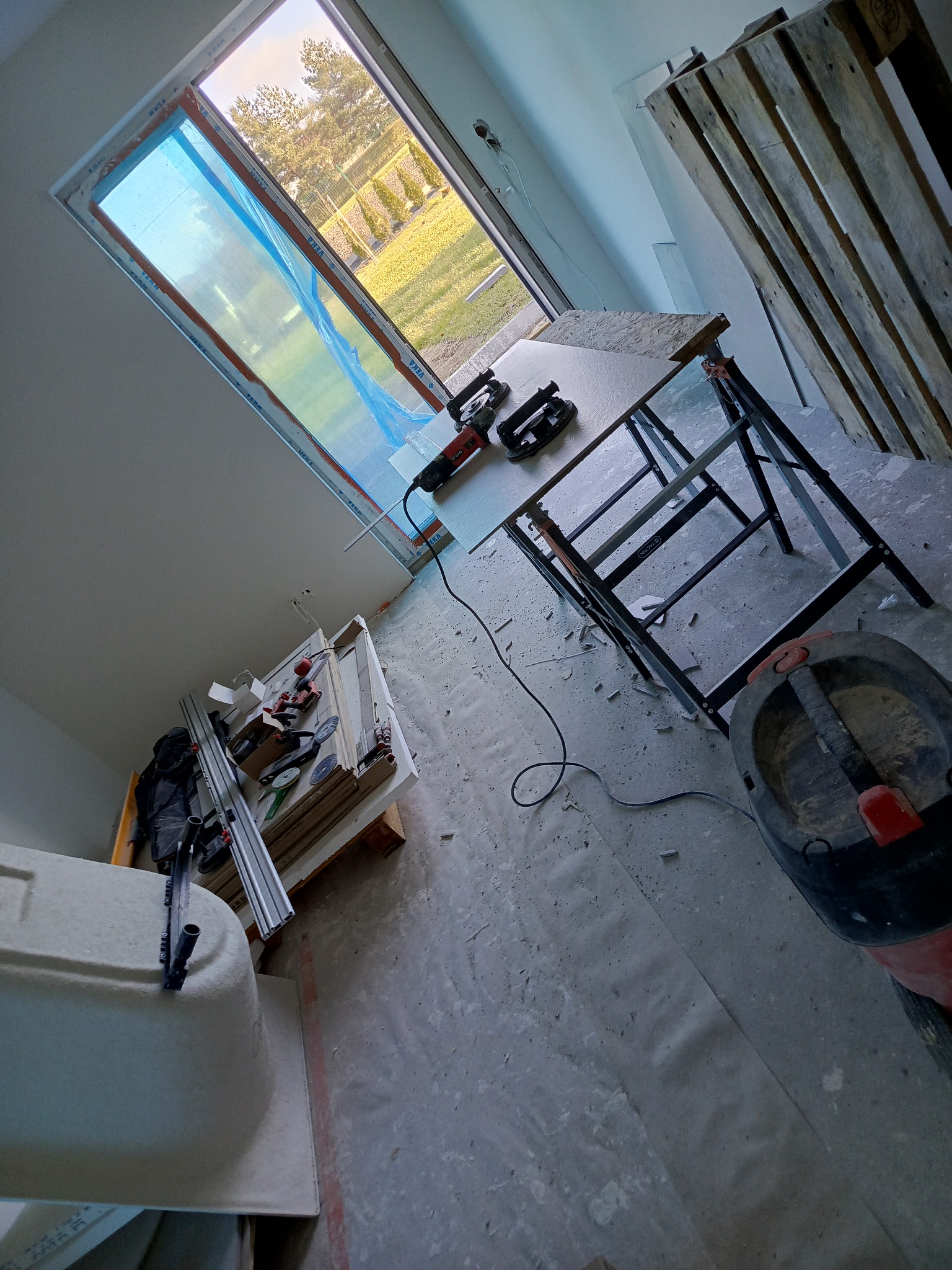 Przygotowania do prac wykończeniowych w Bytomiu. Widoczny stół roboczy z narzędziami, paleta i okno dachowe. Podłoga zabezpieczona folią.